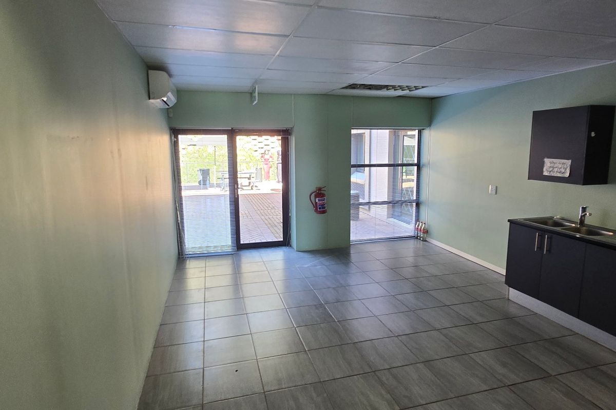 Open-plan commercial space featuring tiled flooring, a drop ceiling, a kitchenette with built-in cabinetry, and direct access to an outdoor patio area.