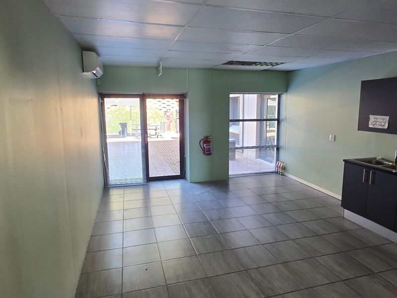 Open-plan commercial space featuring tiled flooring, a drop ceiling, a kitchenette with built-in cabinetry, and direct access to an outdoor patio area.