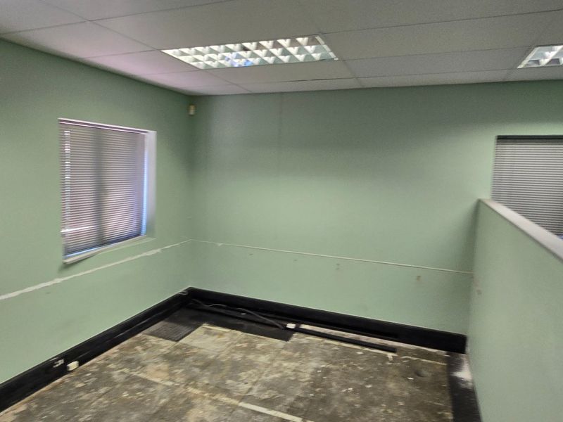 An empty commercial office space featuring a suspended ceiling, recessed lighting, and partition wall, currently requiring flooring and wall finish repairs.
