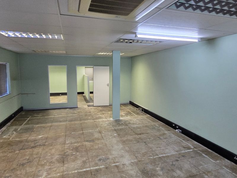 An empty commercial office space featuring a suspended ceiling, recessed lighting, central air conditioning, and exposed flooring ready for refurbishment.