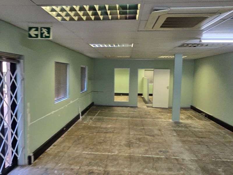 An empty commercial office space featuring a suspended ceiling, recessed lighting, central air conditioning, and a security gate at the entrance.