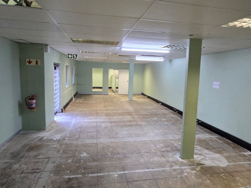 An empty, open-plan commercial office space featuring a suspended ceiling, fluorescent lighting, and a structural support column, ready for tenant fit-out.