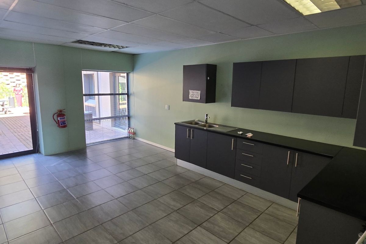 A clean, empty commercial kitchenette featuring dark cabinetry, stainless steel sink, tiled flooring, and direct access to an outdoor patio area.