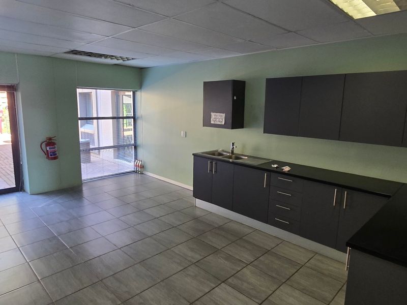A clean, empty commercial kitchenette featuring dark cabinetry, stainless steel sink, tiled flooring, and direct access to an outdoor patio area.