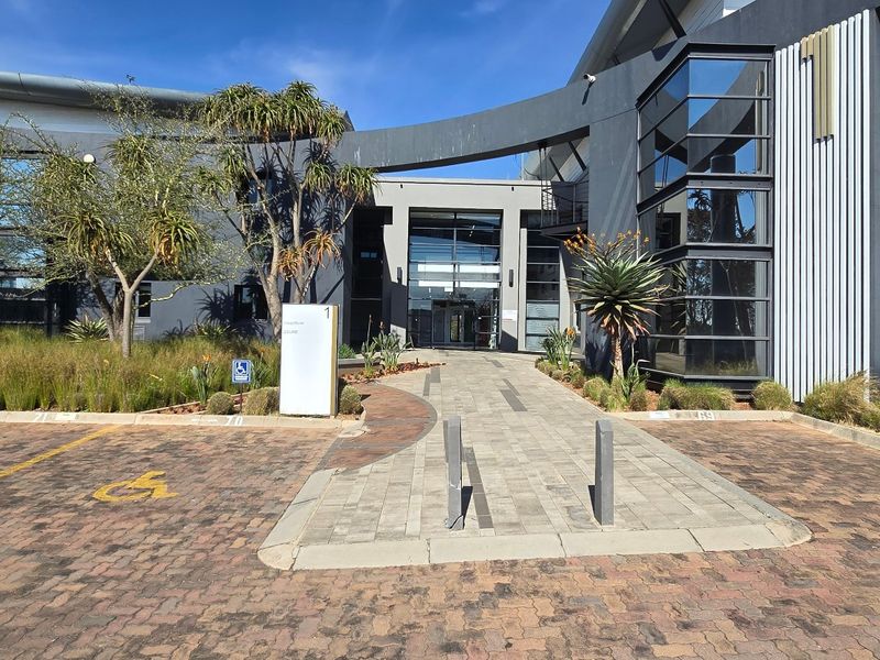 Modern commercial office building entrance featuring contemporary architectural design, glass facade, paved access path, and landscaped surroundings.