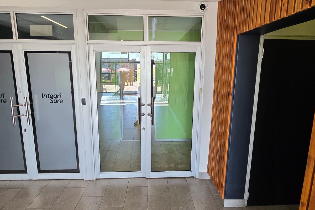 Modern commercial entrance featuring aluminium framed glass double doors, tiled flooring, and decorative timber slat wall cladding.