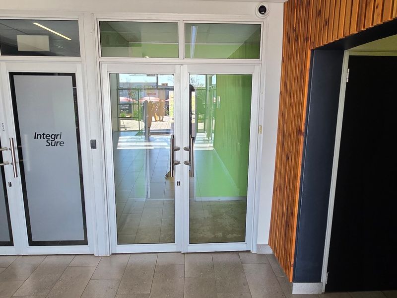 Modern commercial entrance featuring aluminium framed glass double doors, tiled flooring, and decorative timber slat wall cladding.