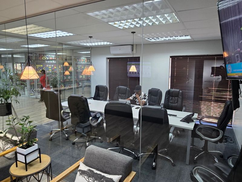 Modern commercial office meeting room featuring glass partitions, suspended ceilings, and integrated air conditioning, providing a professional and well-lit workspace environment.