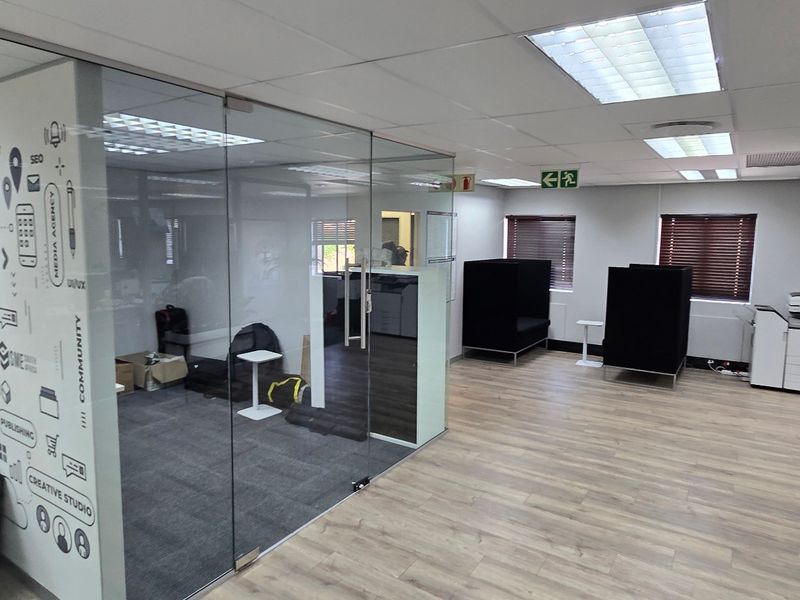 Modern commercial office space featuring glass partitioned rooms, suspended ceilings with recessed lighting, and a combination of laminate and carpet flooring.