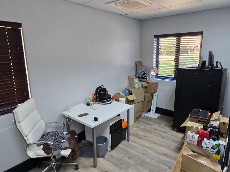 A functional office space featuring laminate flooring, recessed ceiling lighting, and dual windows with venetian blinds, suitable for a professional work environment.