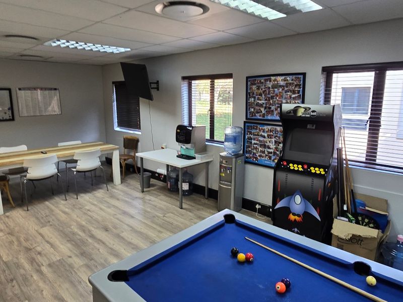 A functional commercial office or break room featuring laminate flooring, suspended ceilings with recessed lighting, and large windows with venetian blinds.