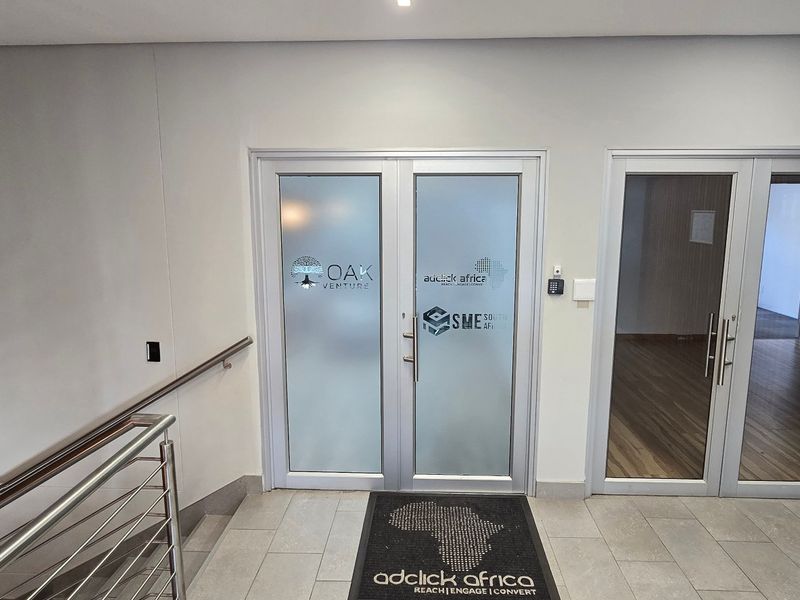 A modern commercial office entrance featuring frosted glass double doors, sleek aluminium frames, and professional access control systems.