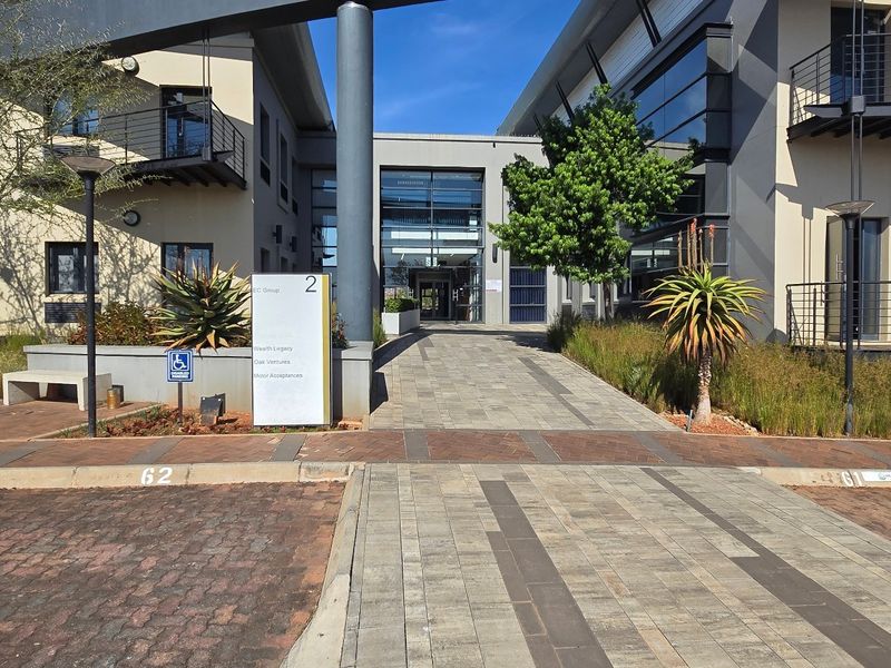 Modern commercial office complex entrance featuring paved walkways, glass facade elements, and professional landscaping with dedicated parking bays.