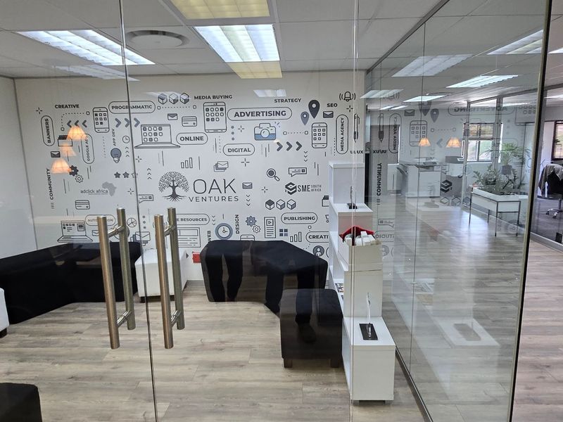 Modern commercial office space featuring glass partitioning, laminate flooring, and a professional open-plan layout with integrated branding elements.