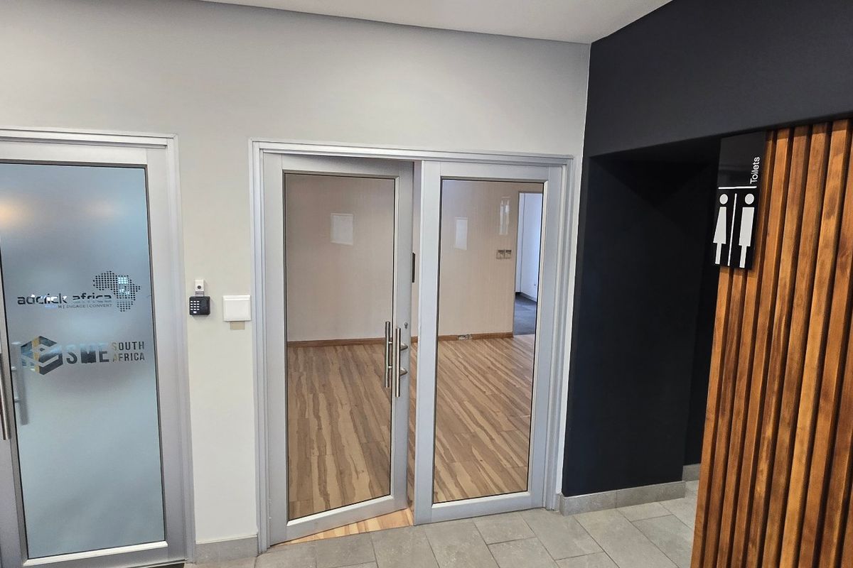Modern commercial office entrance featuring aluminium glass doors, timber slat wall detailing, and a clean, professional aesthetic with access control.