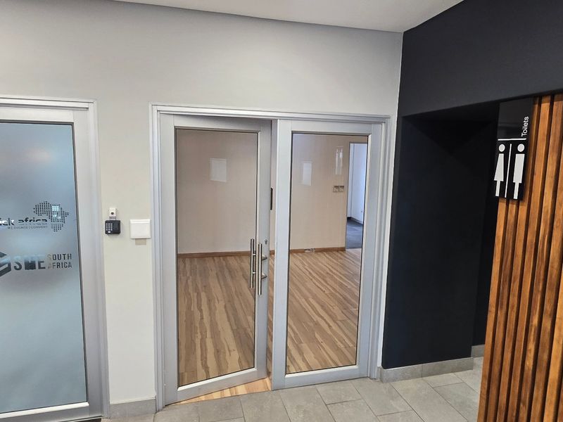 Modern commercial office entrance featuring aluminium glass doors, timber slat wall detailing, and a clean, professional aesthetic with access control.