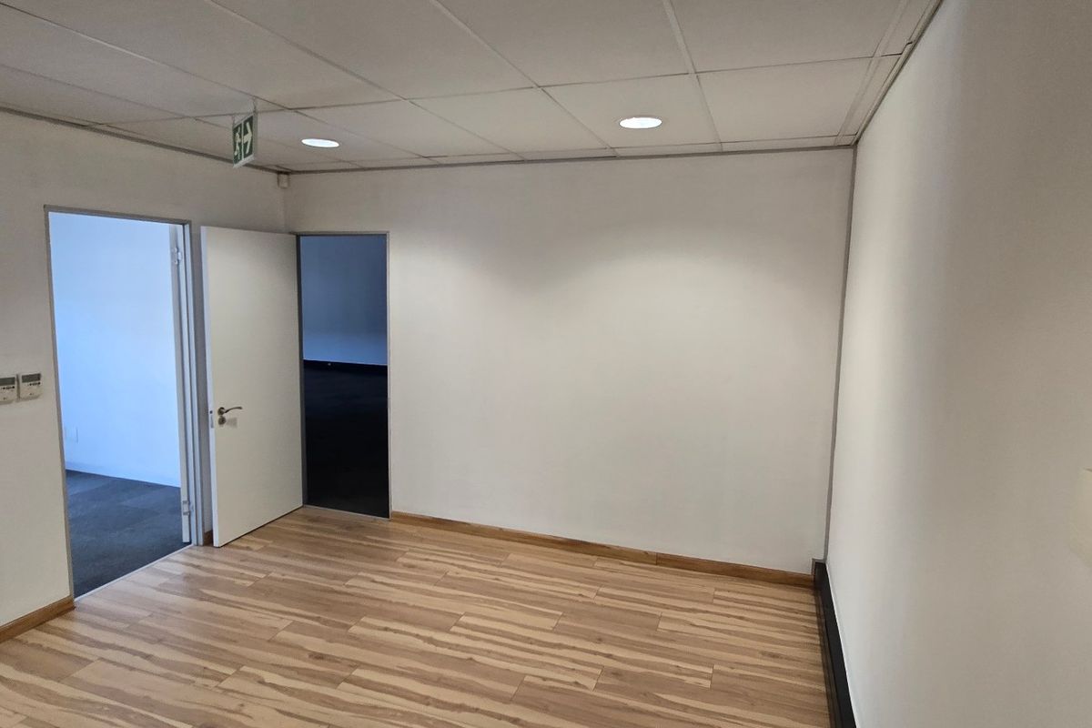 An empty commercial office space featuring laminate flooring, a suspended ceiling with recessed lighting, and multiple internal access points.