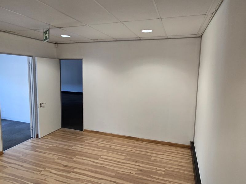 An empty commercial office space featuring laminate flooring, a suspended ceiling with recessed lighting, and multiple internal access points.