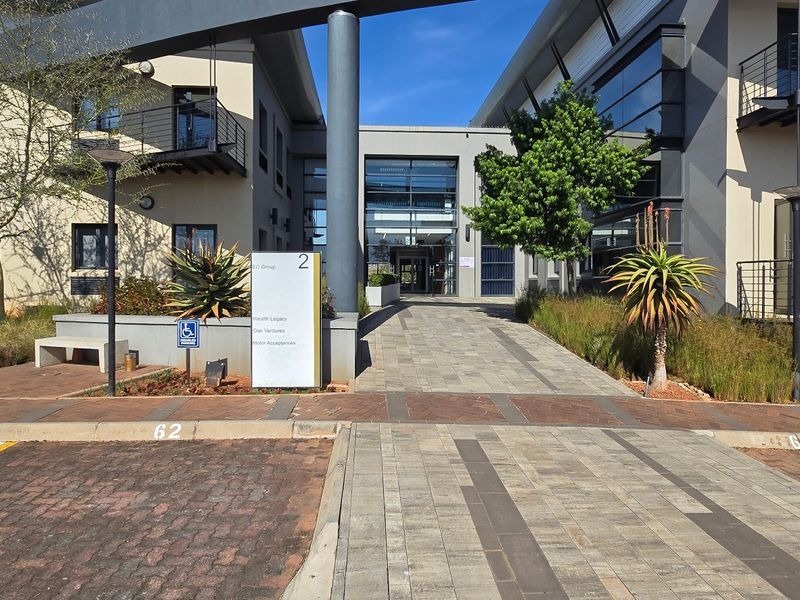 Modern commercial office building entrance featuring a paved walkway, glass facade, and professional signage in a well-maintained business park setting.