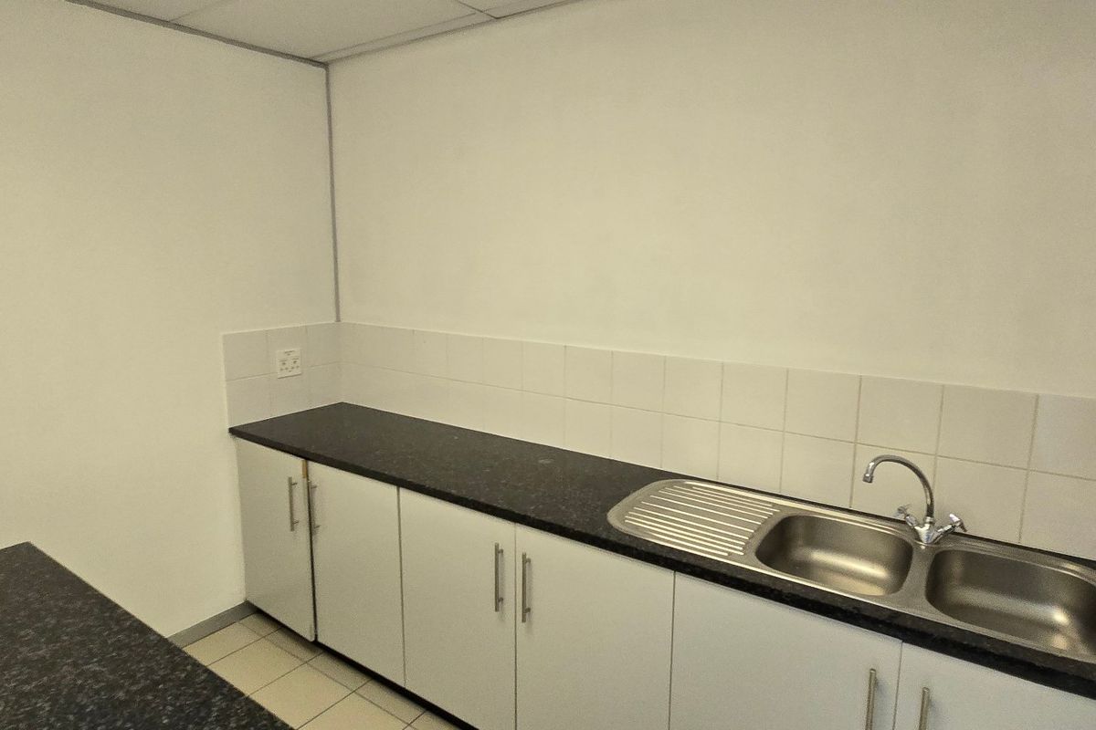 A functional, empty kitchenette featuring white cabinetry, dark laminate countertops, and a stainless steel double sink with a tiled splashback.