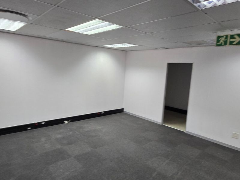 A clean, vacant commercial office space featuring neutral carpet tiles, a suspended ceiling with recessed lighting, and a functional layout.
