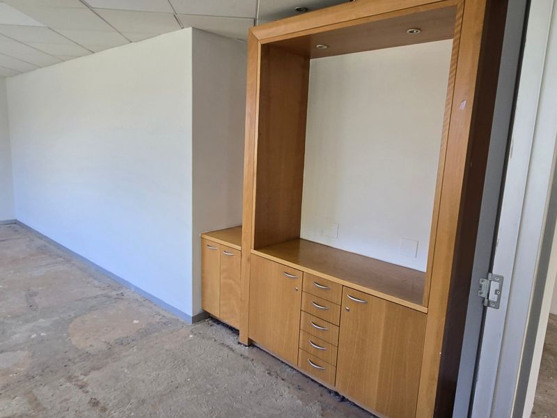 An empty commercial office space featuring built-in wooden cabinetry, recessed ceiling lighting, and unfinished concrete flooring, ready for renovation or fit-out.