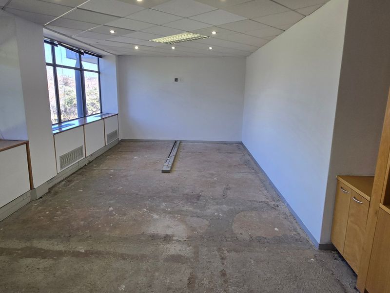 An empty office space featuring large windows, built-in cabinetry, and a suspended ceiling, currently requiring new flooring installation.