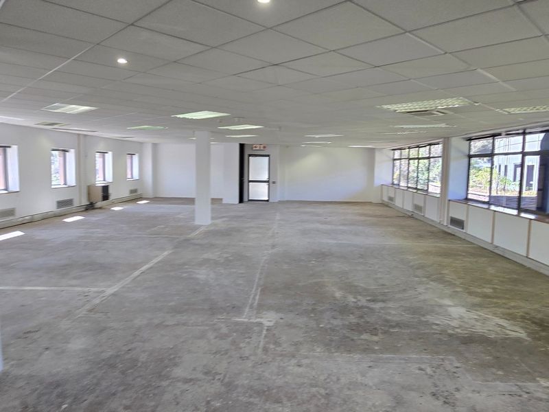 A large, open-plan commercial office space featuring a suspended ceiling, recessed lighting, and expansive windows, currently awaiting flooring installation and final fit-out.