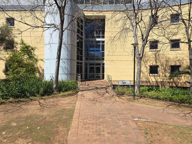 Front exterior view of a commercial office building featuring a brick facade, central glass entrance, and a paved walkway leading to the main door.