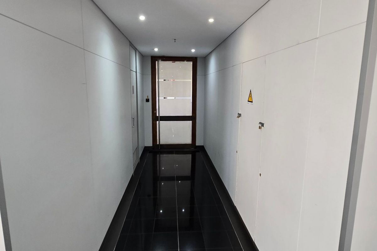 A clean, modern commercial hallway featuring high-gloss black floor tiles, minimalist white wall paneling, and recessed ceiling lighting leading to a glass-paneled door.