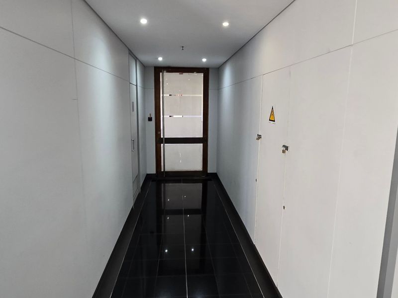 A clean, modern commercial hallway featuring high-gloss black floor tiles, minimalist white wall paneling, and recessed ceiling lighting leading to a glass-paneled door.