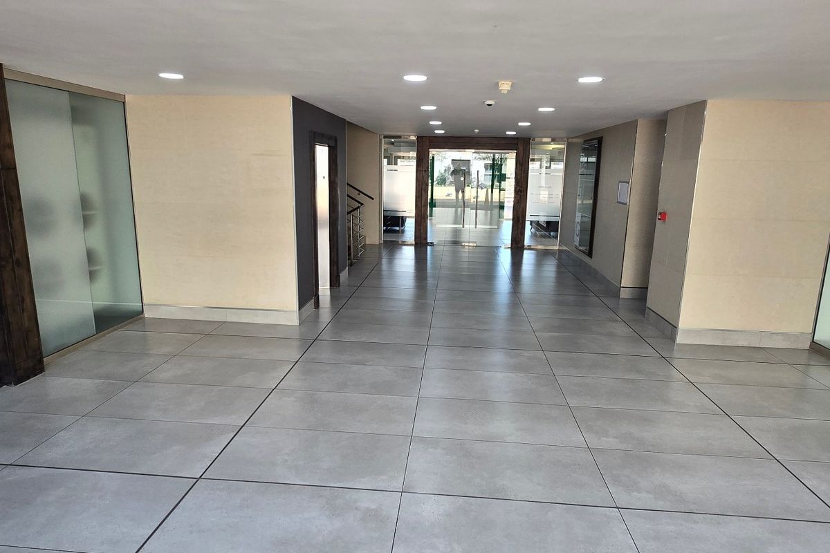 A modern, spacious commercial building entrance lobby featuring large format floor tiles, recessed lighting, and glass partition walls.