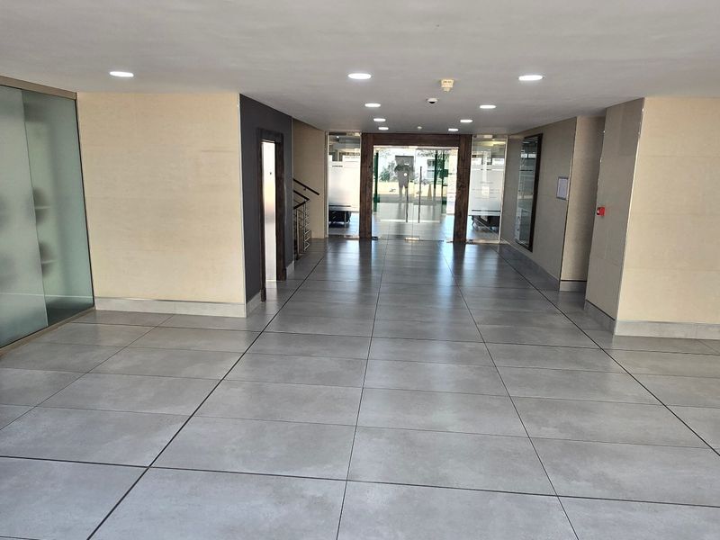 A modern, spacious commercial building entrance lobby featuring large format floor tiles, recessed lighting, and glass partition walls.