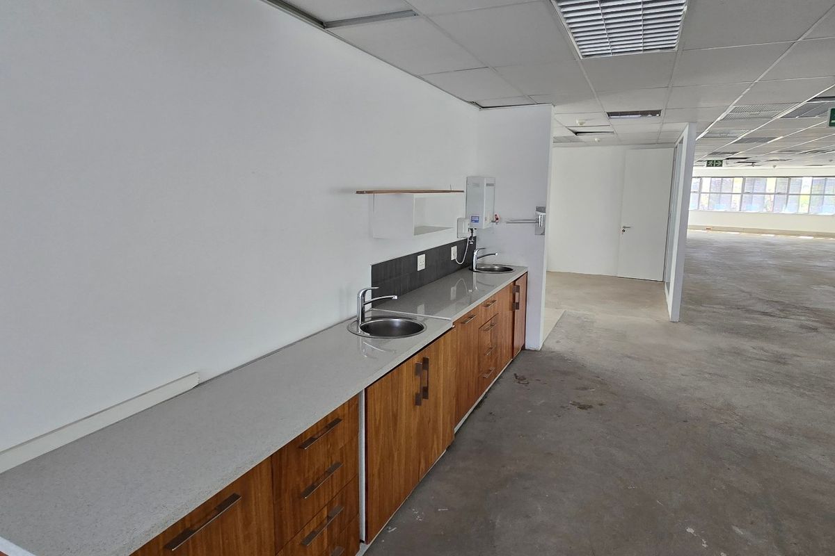 A functional kitchenette area featuring wood-finish cabinetry, stone countertops, and a stainless steel sink, set within an open-plan commercial office space.