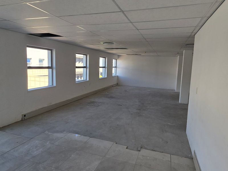 An empty, open-plan commercial office space featuring large windows, a suspended ceiling, and tiled flooring, ready for custom fit-out.