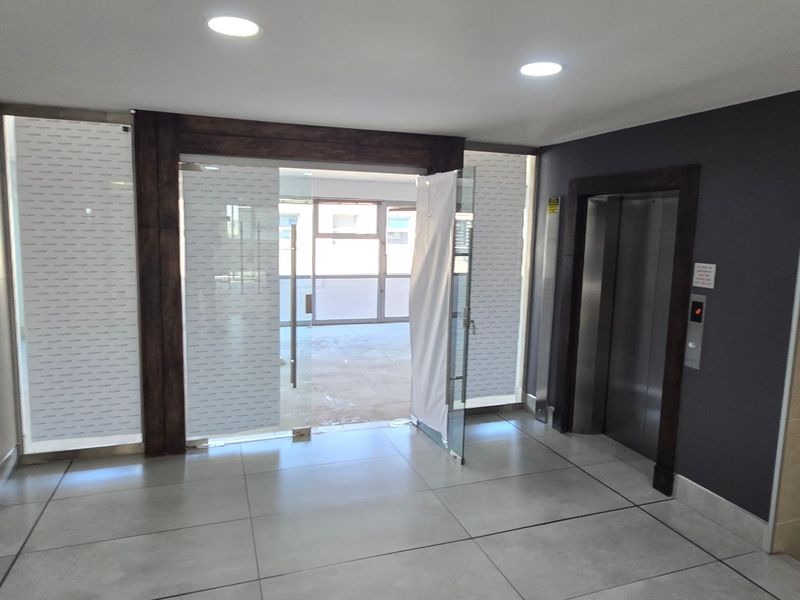 Modern commercial building entrance lobby featuring tiled flooring, recessed lighting, a glass entry door, and elevator access.
