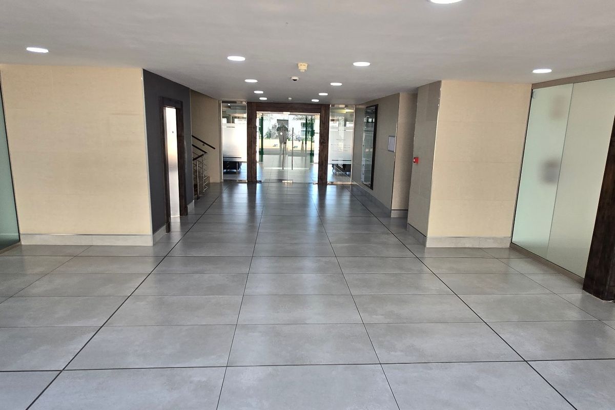 A spacious and modern commercial entrance lobby featuring large format floor tiles, recessed lighting, and glass partition walls leading to the main entrance.