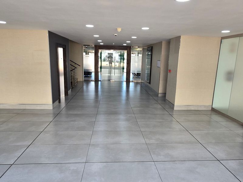 A spacious and modern commercial entrance lobby featuring large format floor tiles, recessed lighting, and glass partition walls leading to the main entrance.