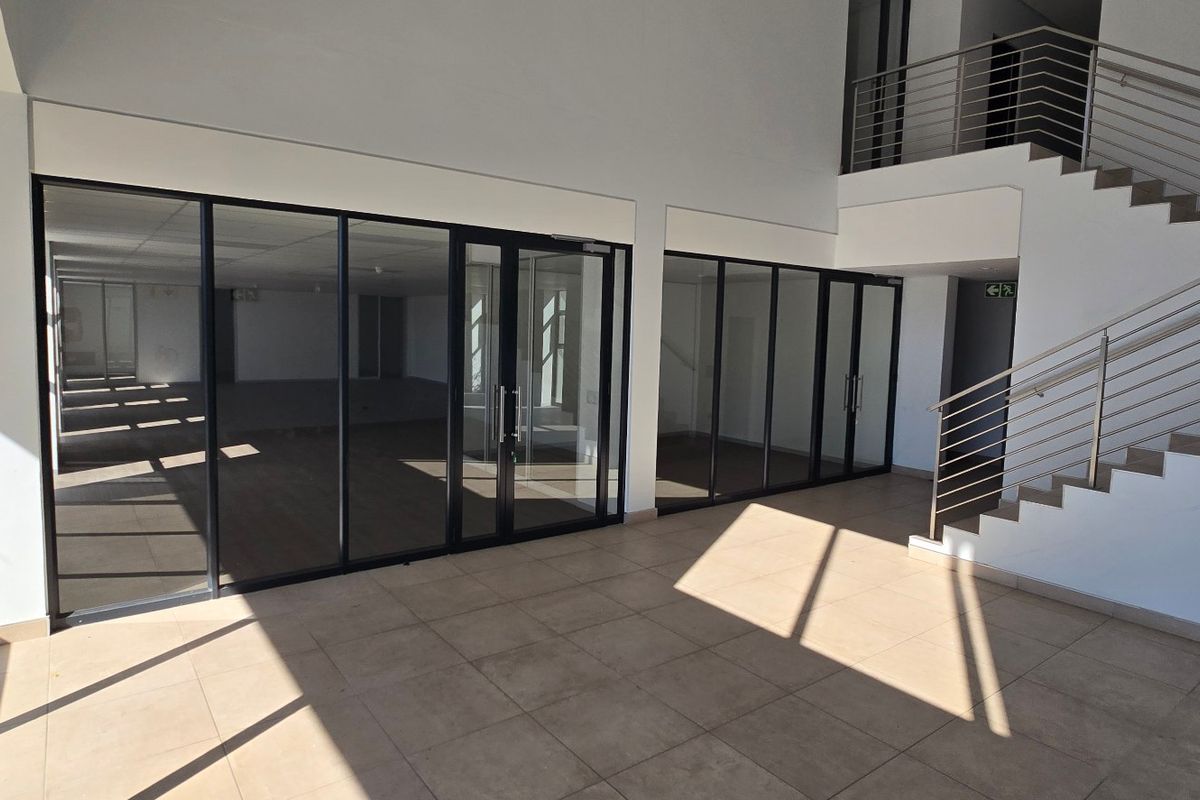 Modern industrial entrance foyer featuring tiled flooring, a staircase with stainless steel balustrades, and extensive aluminium-framed glass partitioning.