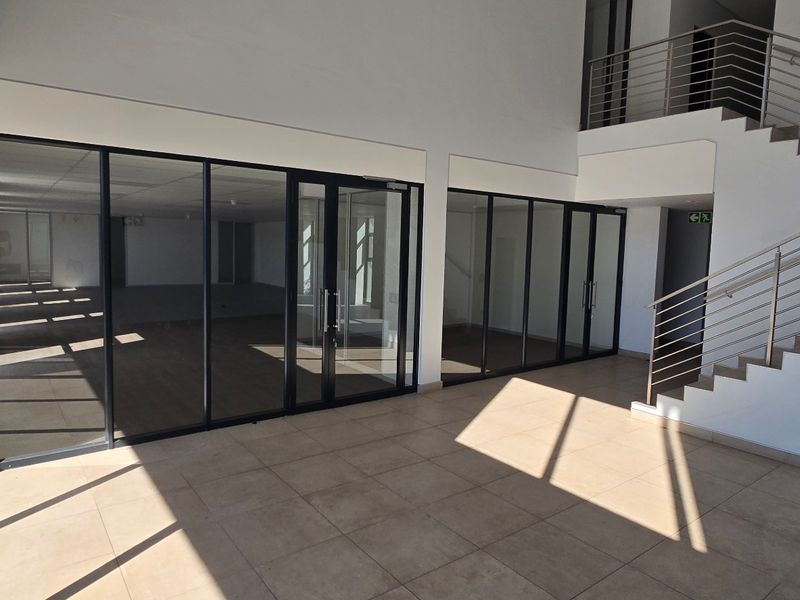 Modern industrial entrance foyer featuring tiled flooring, a staircase with stainless steel balustrades, and extensive aluminium-framed glass partitioning.