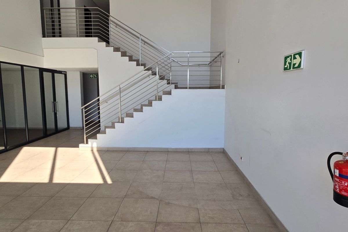 Spacious industrial entrance foyer featuring tiled flooring, a modern staircase with stainless steel balustrades, and integrated safety equipment.