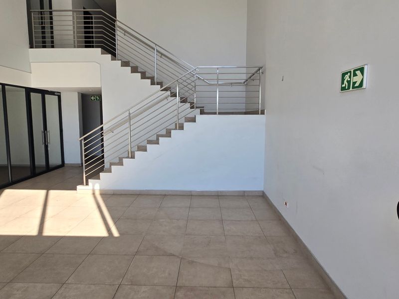 Spacious industrial entrance foyer featuring tiled flooring, a modern staircase with stainless steel balustrades, and integrated safety equipment.