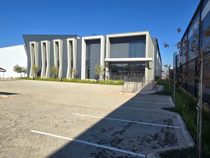 Modern industrial building exterior featuring a paved parking area, covered parking bays, and a contemporary glass and metal facade.