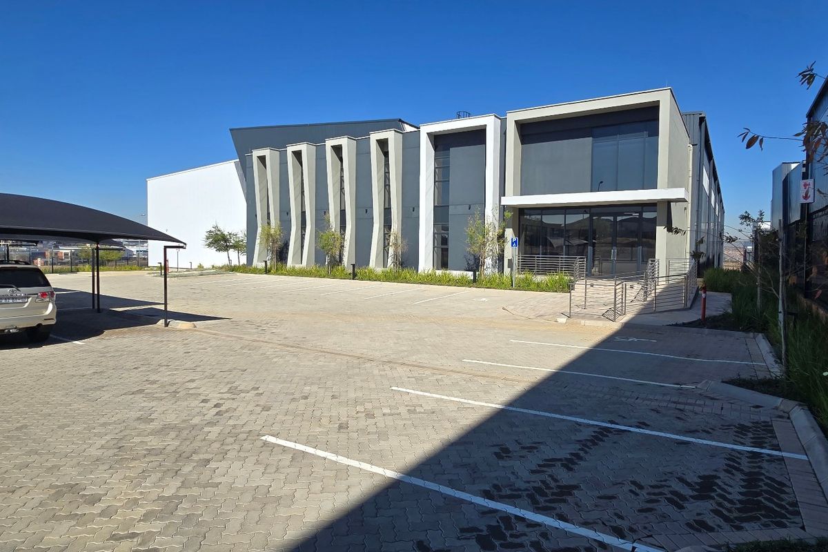 Modern industrial building exterior featuring a paved parking area, shade cloth carport, and contemporary architectural facade with glass entrance.