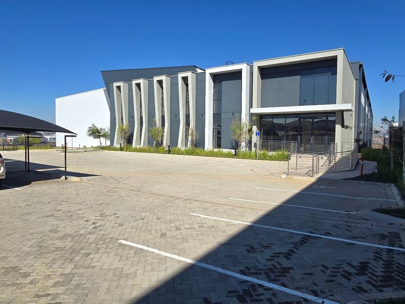 Modern industrial building exterior featuring a paved parking area, shade cloth carport, and contemporary architectural facade with glass entrance.