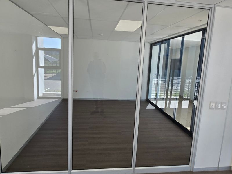 A bright, modern office space featuring glass partition walls, laminate flooring, and a clean, open layout suitable for professional use.