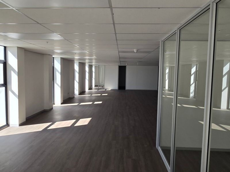 Spacious open-plan office area featuring modern laminate flooring, suspended ceilings, and glass partition walls, offering a bright and professional workspace.