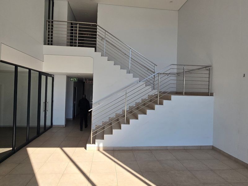 Spacious industrial entrance foyer featuring a modern staircase with stainless steel balustrades, tiled flooring, and large glass partition walls.