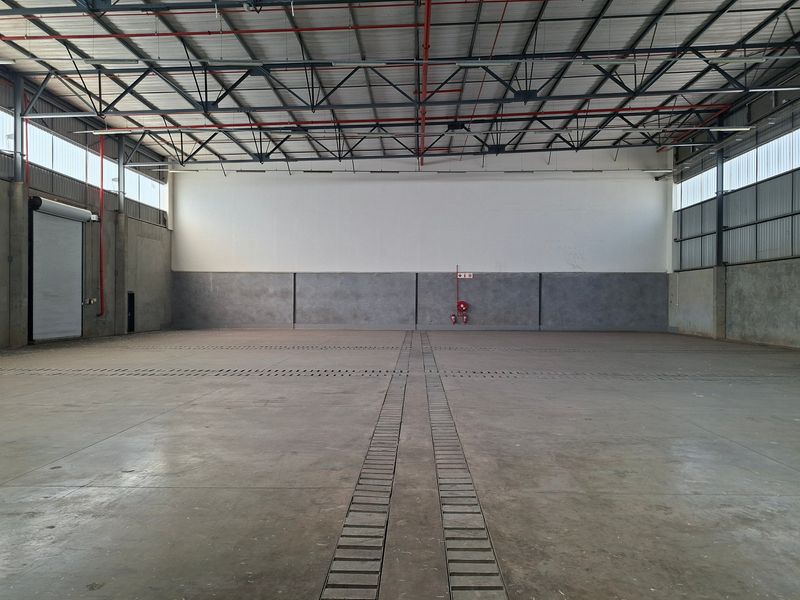 Spacious industrial warehouse featuring high ceilings with exposed steel trusses, concrete flooring, roller shutter access, and integrated fire safety systems.