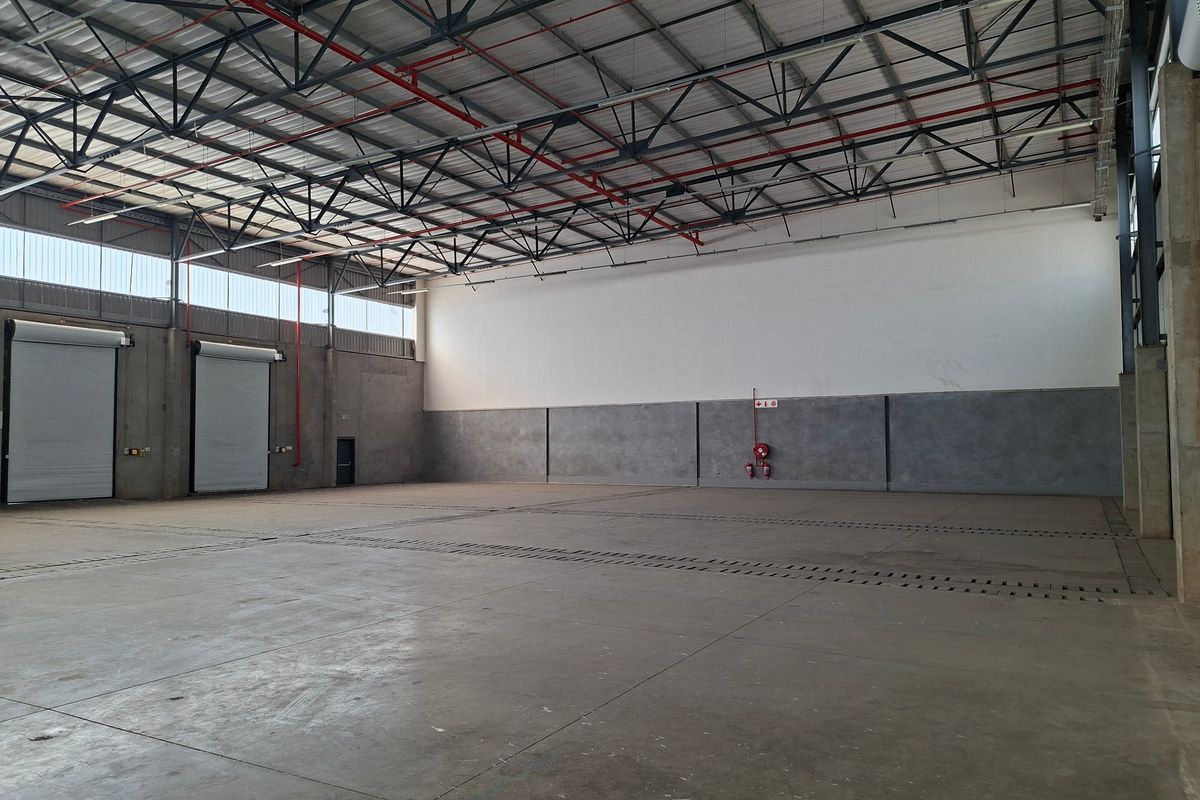 Spacious industrial warehouse unit featuring high ceilings with exposed steel trusses, concrete flooring, and multiple roller shutter doors for efficient access.